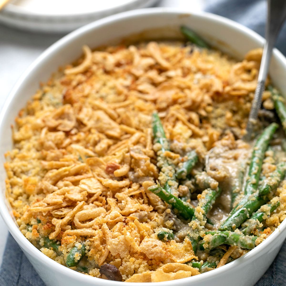 gluten free green bean casserole in large white casserole dish with crispy topping and spoon