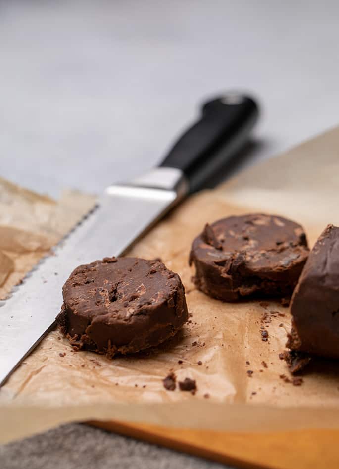 Bread knife on cutting board with 2 disks of brown cookie dough and the rest of the log