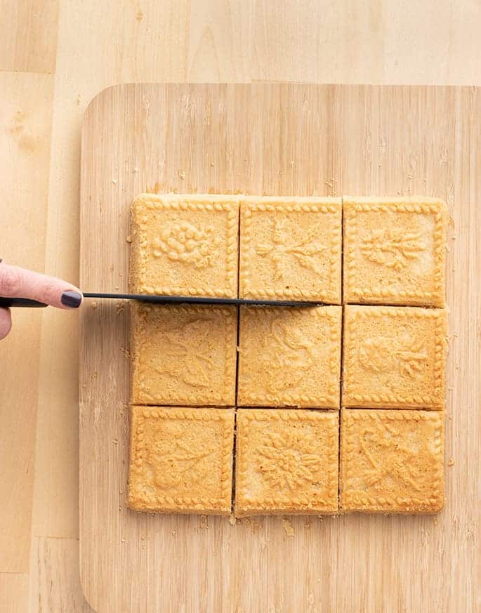 Hand holding a knife cutting apart squares of shortbread on cutting board