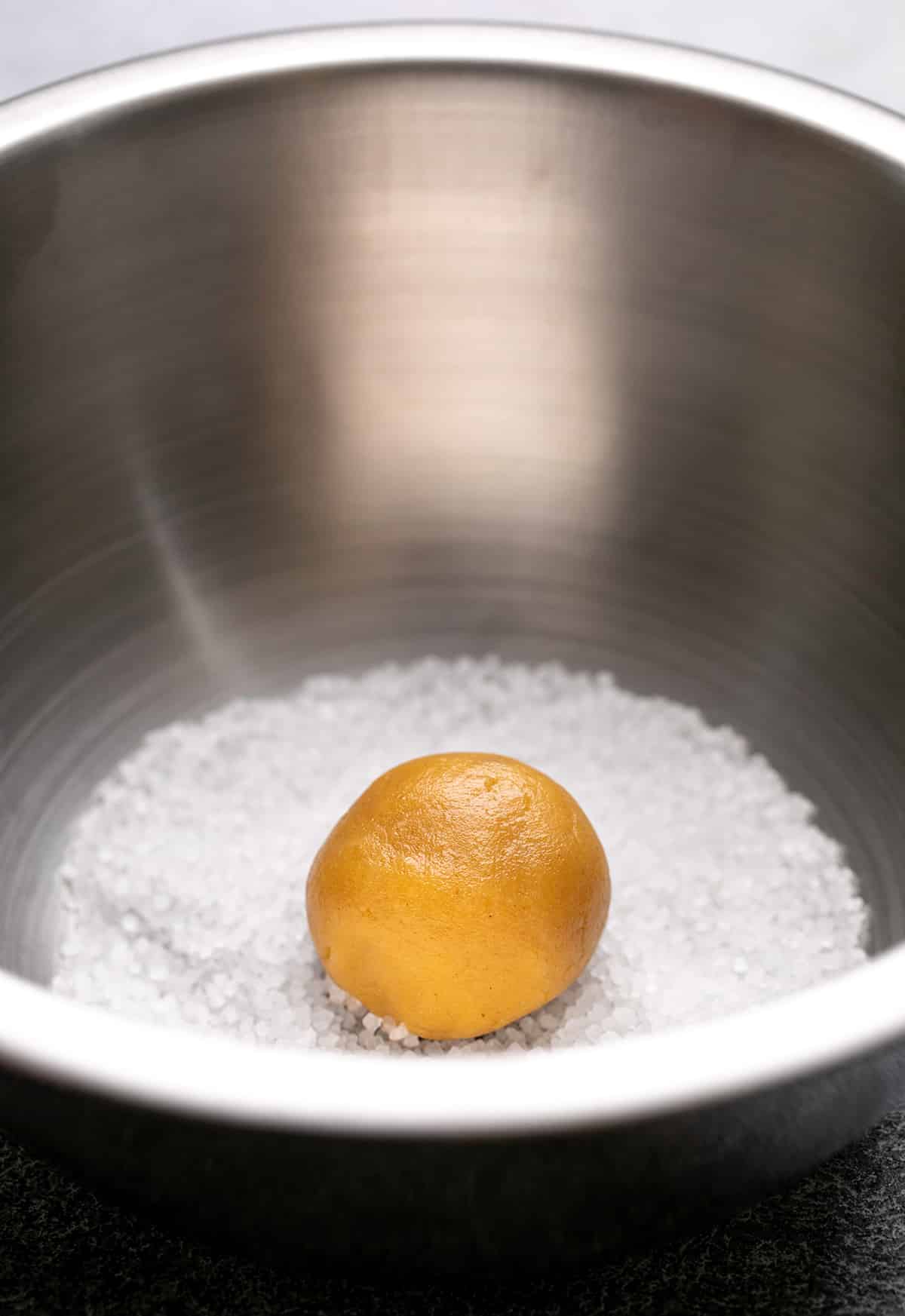 Raw ball of peanut butter cookie dough in coarse sugar in metal bowl