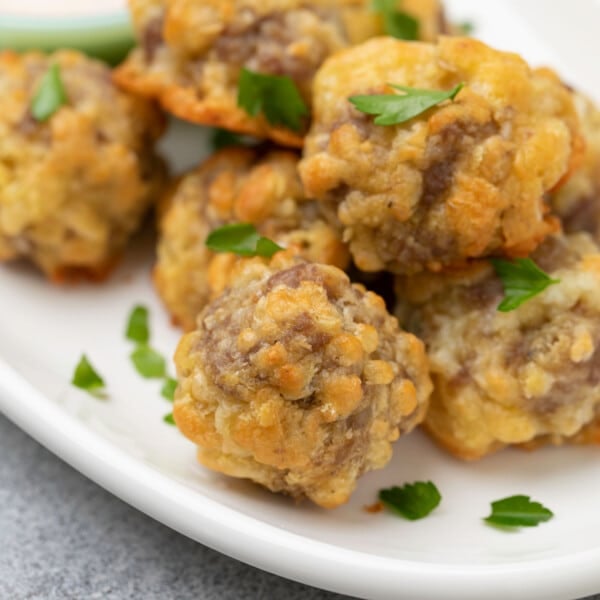 7 gluten free sausage balls on white platter with torn fresh parsley