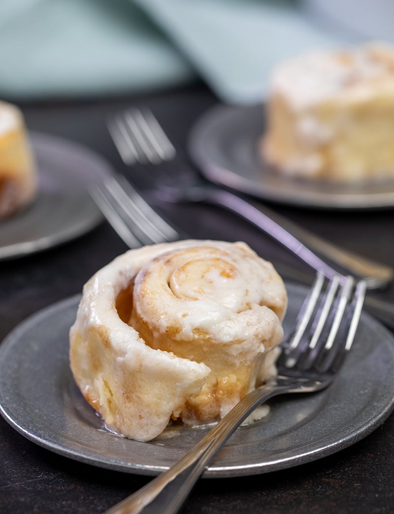 Baked and frosted gluten free cinnamon roll on small round metal plate with fork