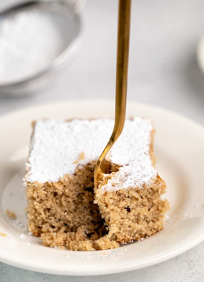 Fork taking a corner of a piece of spice cake on a white plate