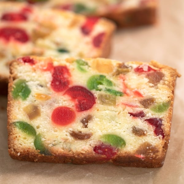 slices of gluten free fruit cake with red and green candied fruits on brown paper