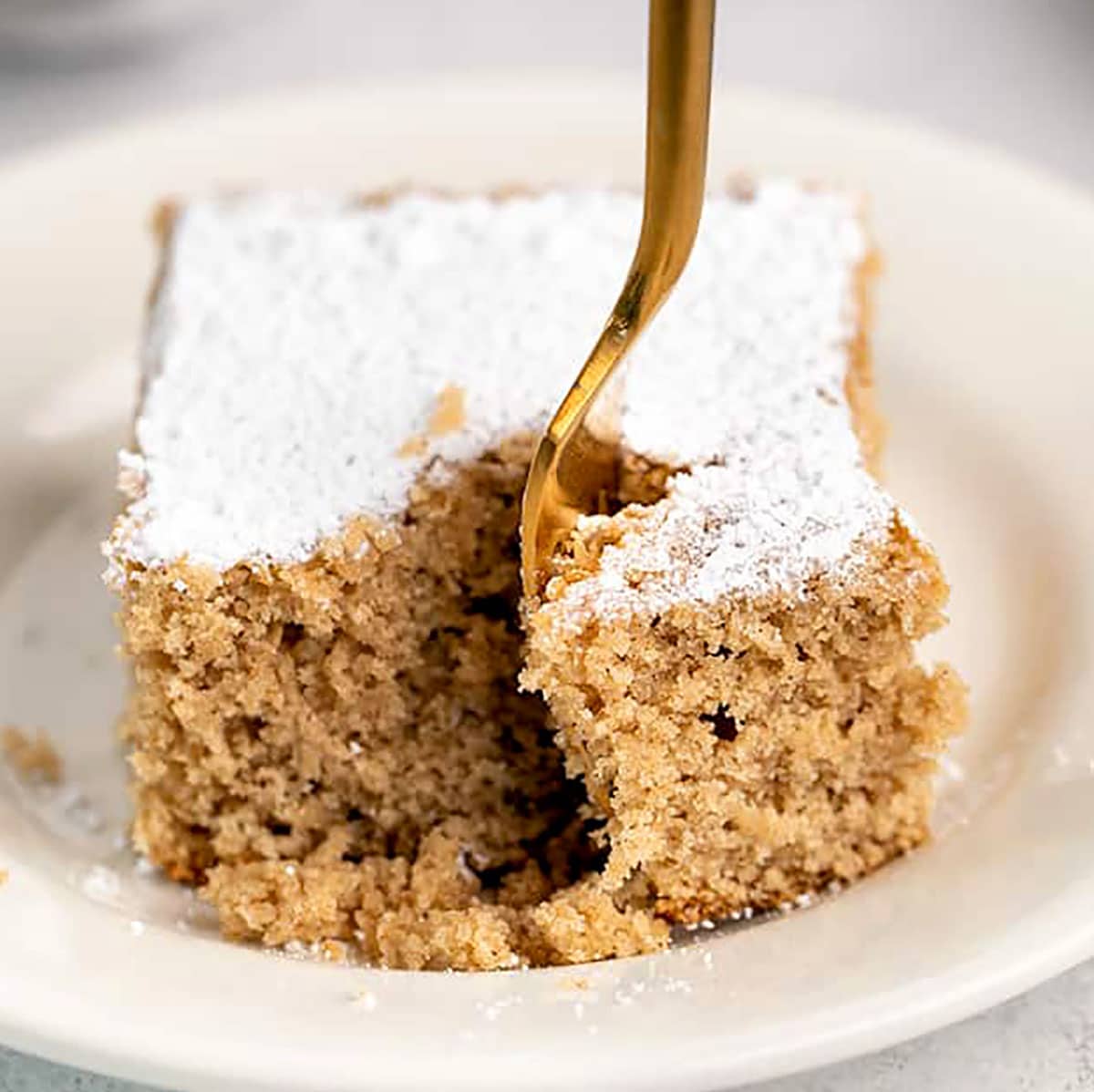 gluten free spice cake with powdered sugar on top with gold fork taking bite away