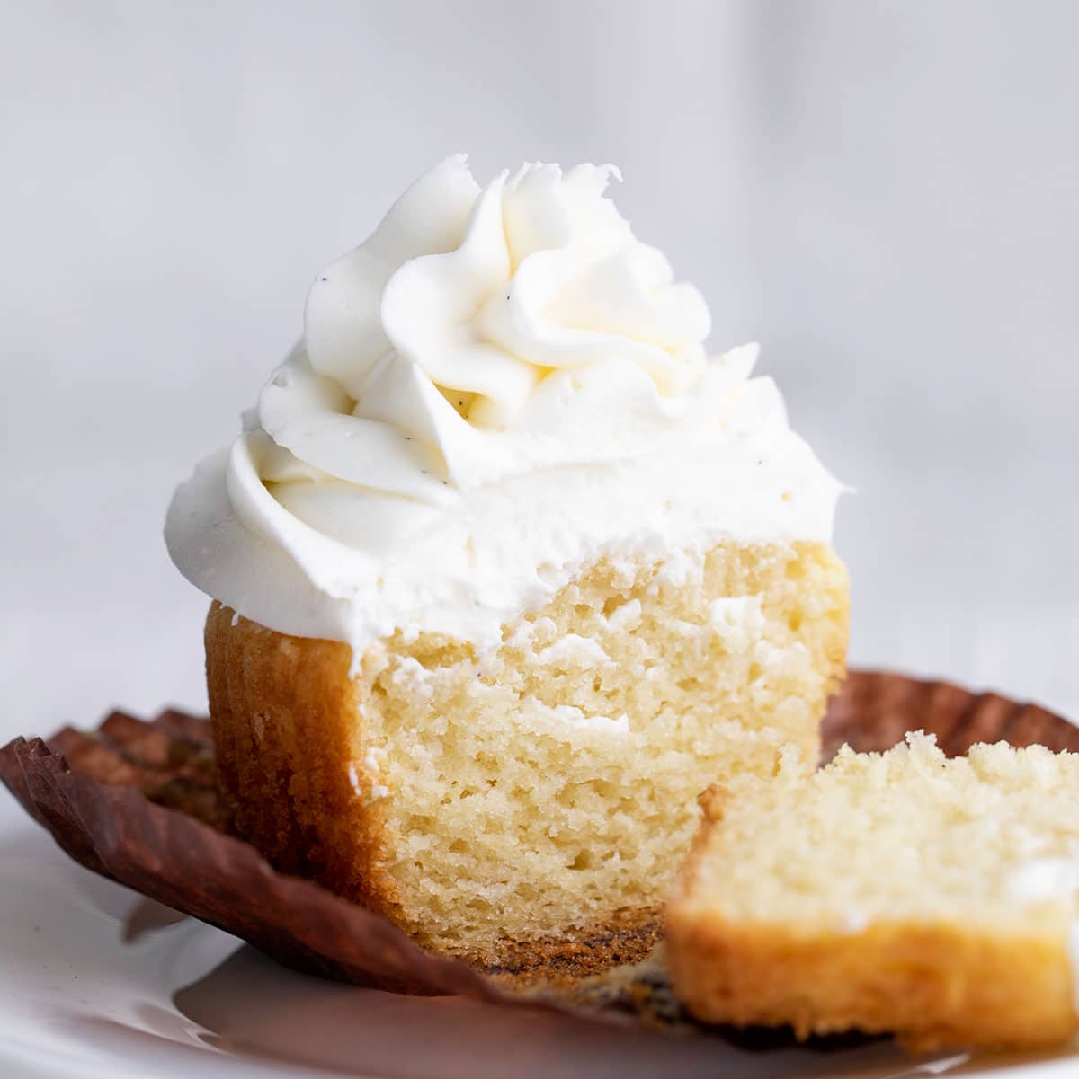 gluten free vanilla cupcake with white swirl of frosting sliced to reveal inside