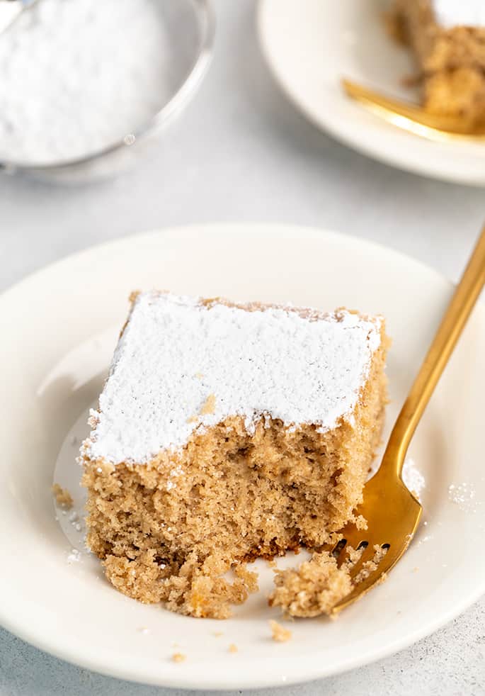 Piece of spice cake on small white plate with fork and bite taken