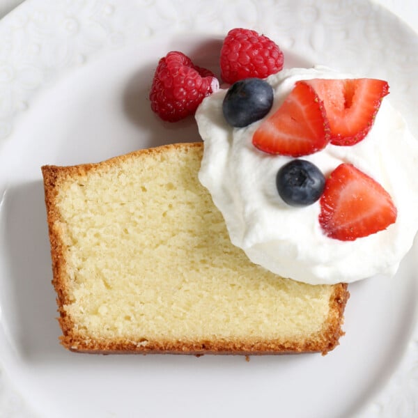 slice of gluten free pound cake with berries and cream on white plate