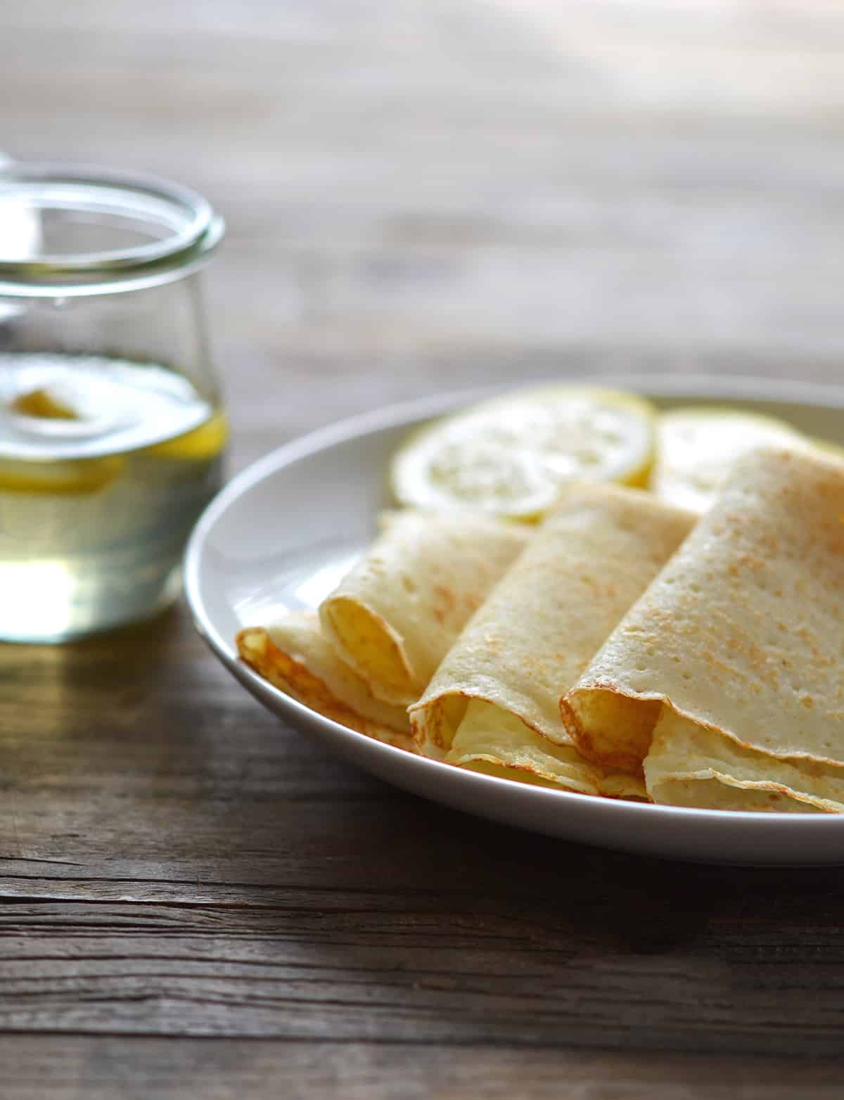 white plate with 4 folded crepes and lemon slices