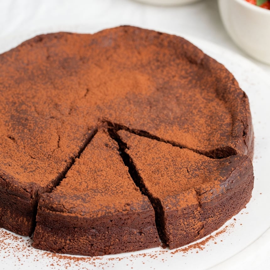 Brown flourless chocolate cake with cocoa powder on top with 2 slices cut