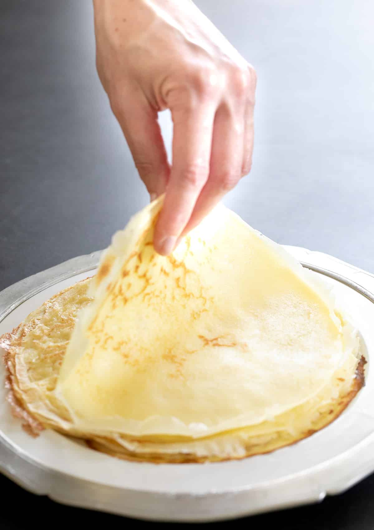 Fingers picking up gluten free crepe from a white plate