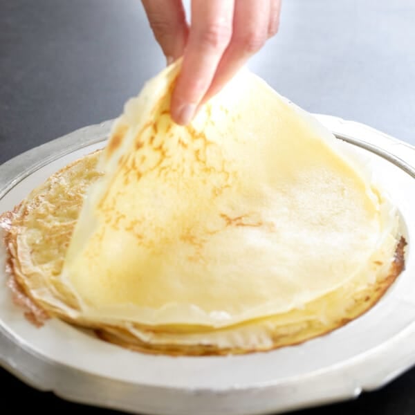 fingers picking up top gluten free crepe from stack on large white plate