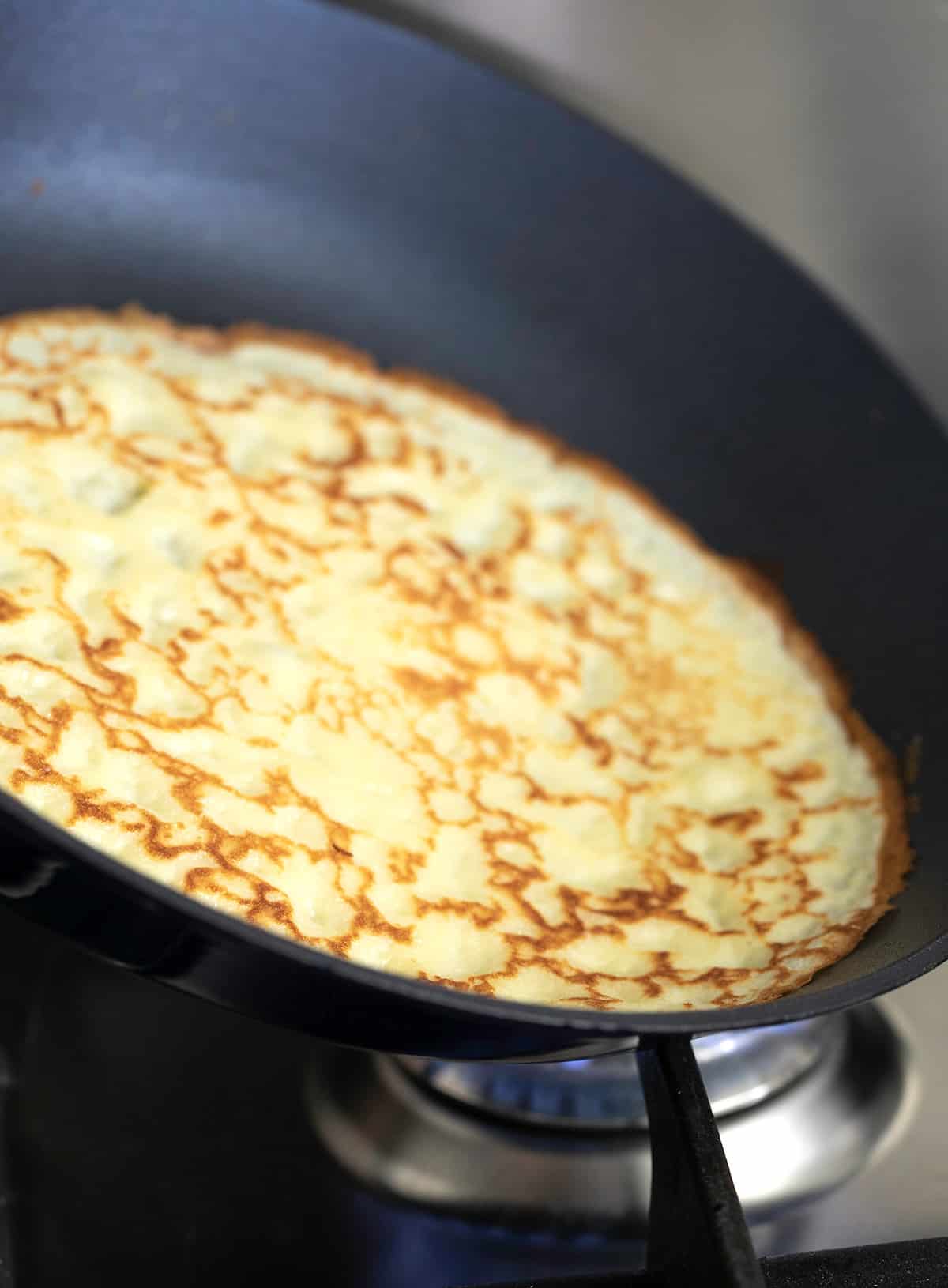 Gluten free crepes sliding from round dark nonstick pan