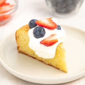 slice of yellow gluten free olive oil cake on white plate with whipped cream and berries