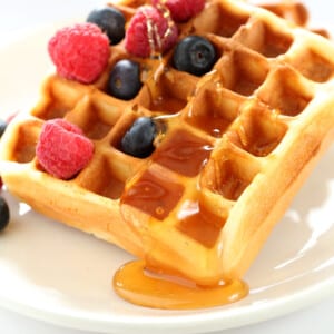 gluten free waffles on white plate with berries and maple syrup