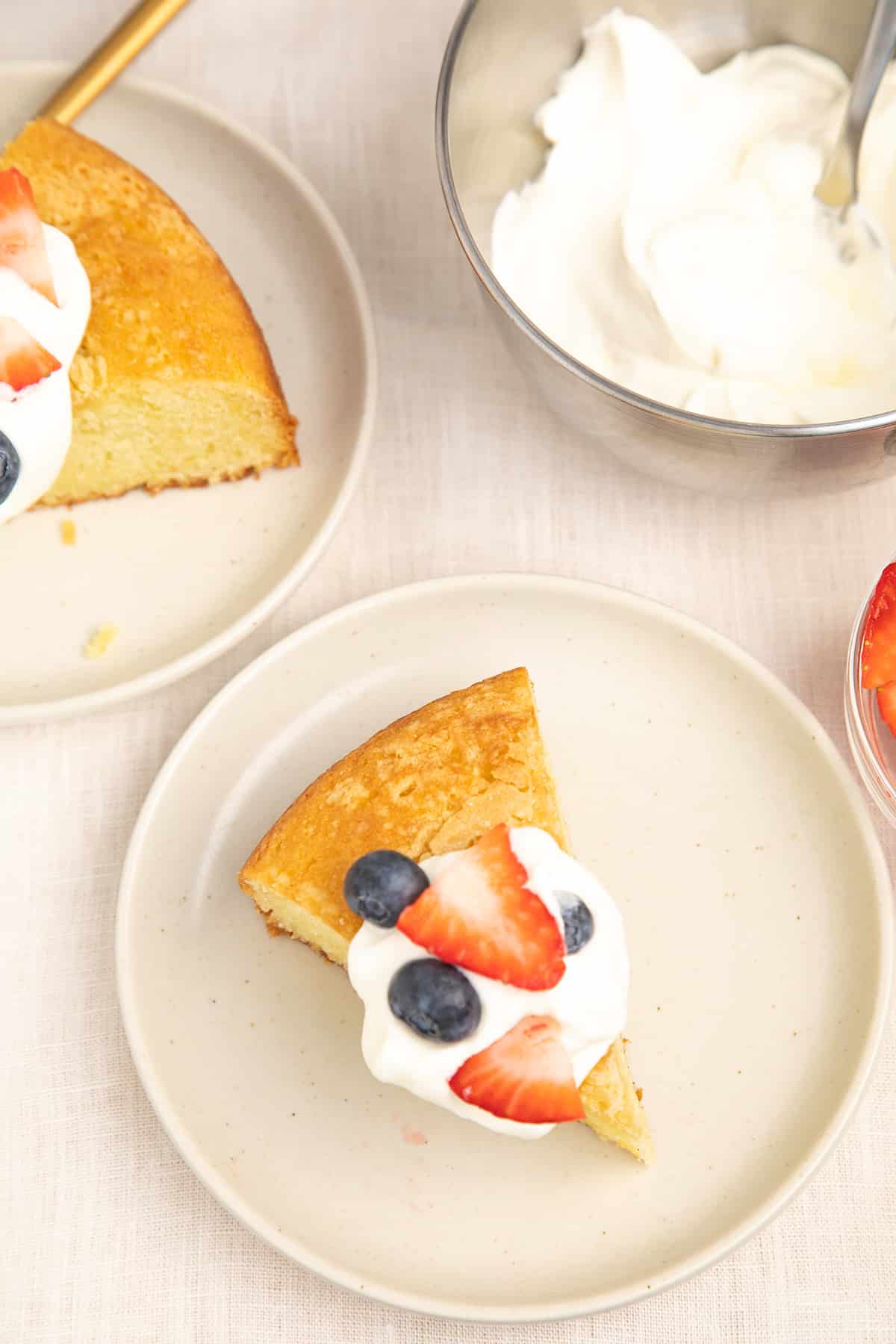 Overhead image of slices of olive oil cake with berries and cream on small white plates