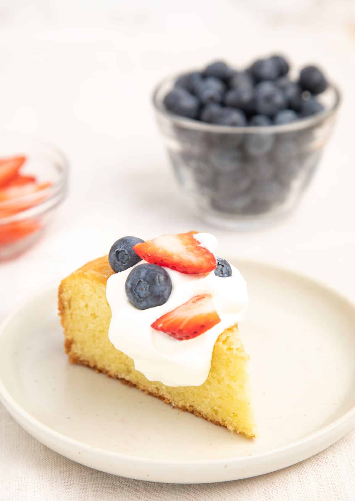 A slice of gluten free olive oil cake served with berries and cream.