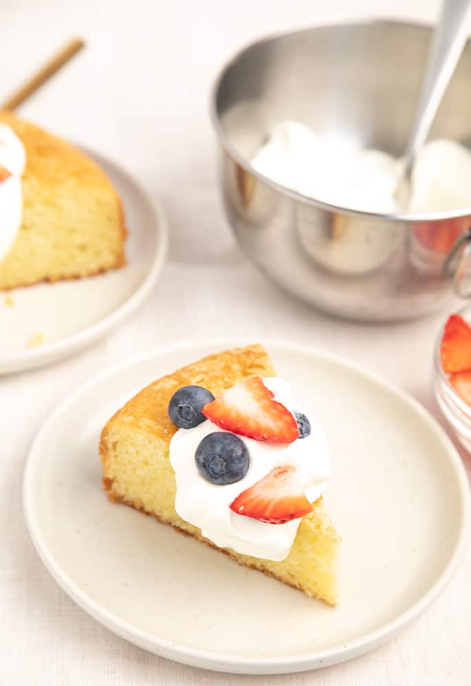 Three-quarter image of slice of olive oil cake with berries and cream