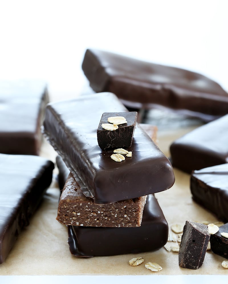 stack of 3 homemade protein bars two covered in chocolate with a piece of chocolate on top