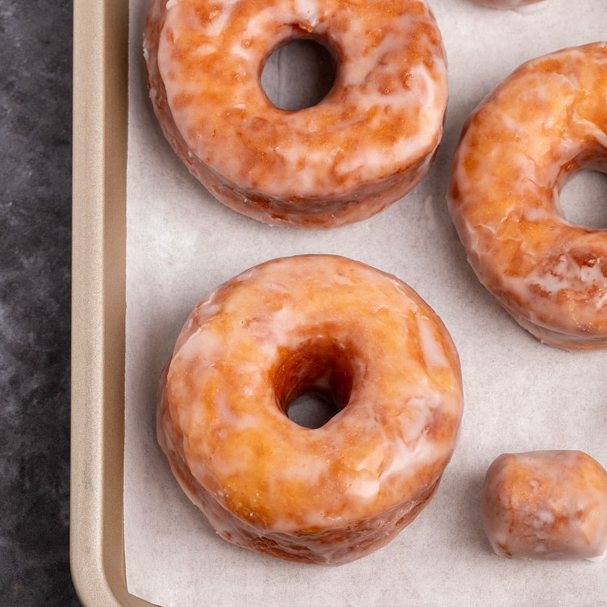 3 brown gluten free donuts with white glaze on white paper on gold baking sheet