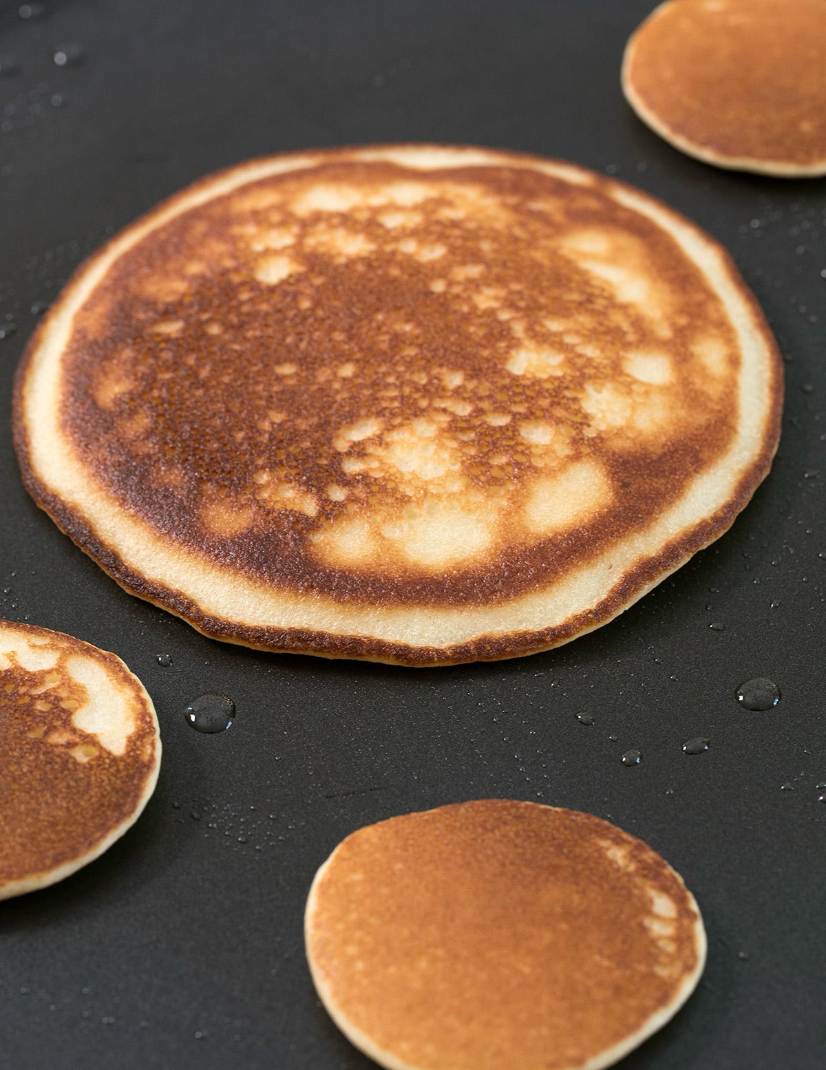 1 large and 3 small browned pancakes cooking on black griddle