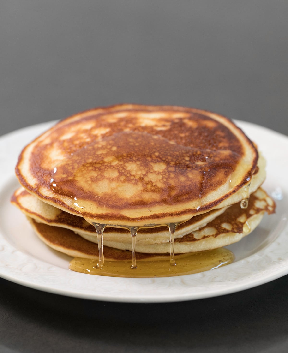 small stack of brown just-cooked Paleo pancakes dripping syrup on a small white plate
