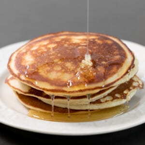 Stack of 5 Paleo pancakes with syrup drizzling on white plate