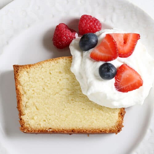 slice of gluten free pound cake with berries and whipped cream on small white plate