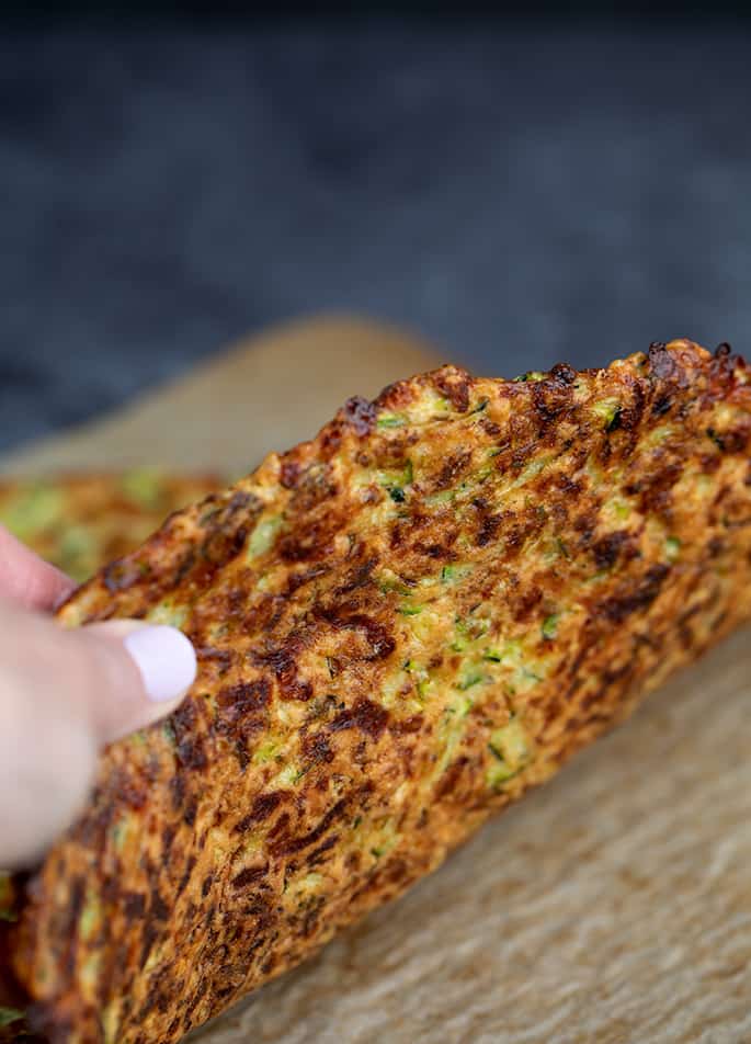 Fingers holding zucchini pizza crust showing underside of baked crust