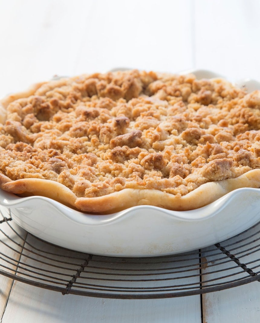 Freshly baked whole apple crumb pie in a white ceramic pie dish, with a golden crust and crisp, browned topping.