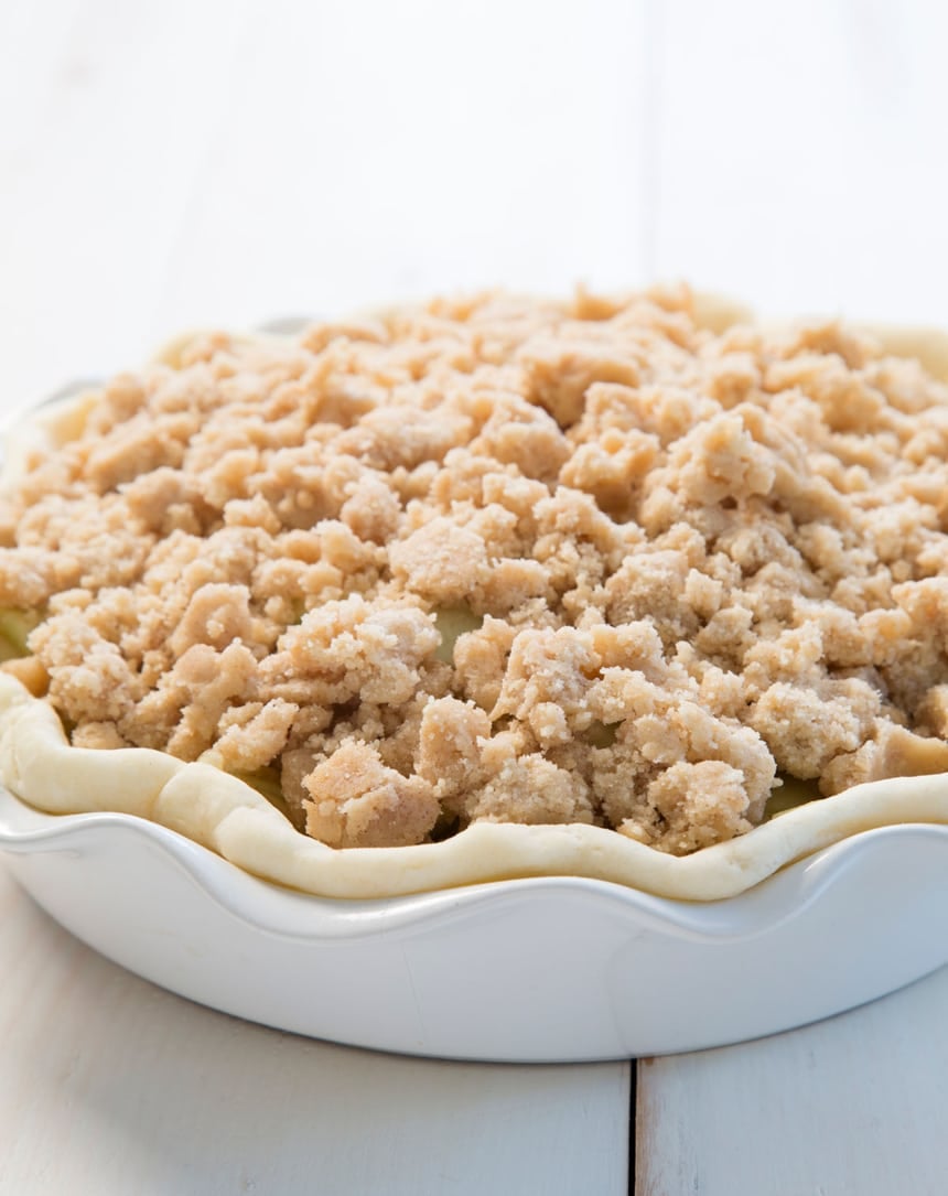 Parbaked pie crust filled with apple slices and covered with a generous layer of crumb topping, ready to go in the oven.