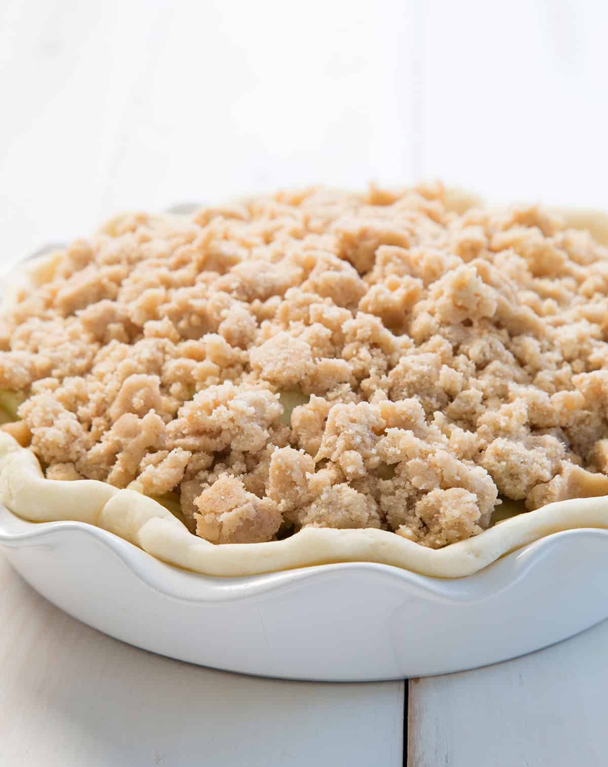 Parbaked pie crust filled with apple slices and covered with a generous layer of crumb topping, ready to go in the oven.