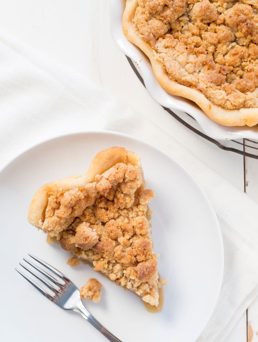 Overhead view of a slice of gluten free apple pie on a plate next to the full pie in its baking dish.
