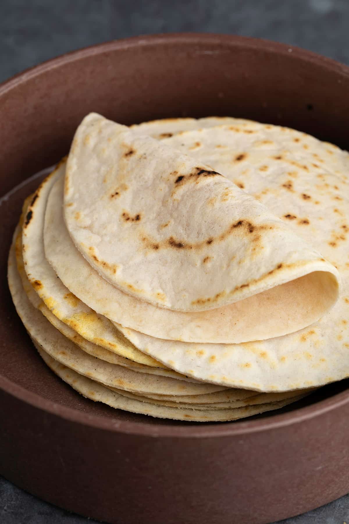 Stack of cassava flour tortillas with one folded on top in brown tortilla warmer