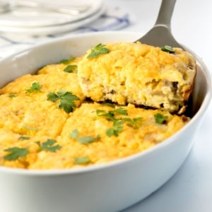metal spatula holding rectangle of yellow breakfast casserole lifting out of white casserole dish