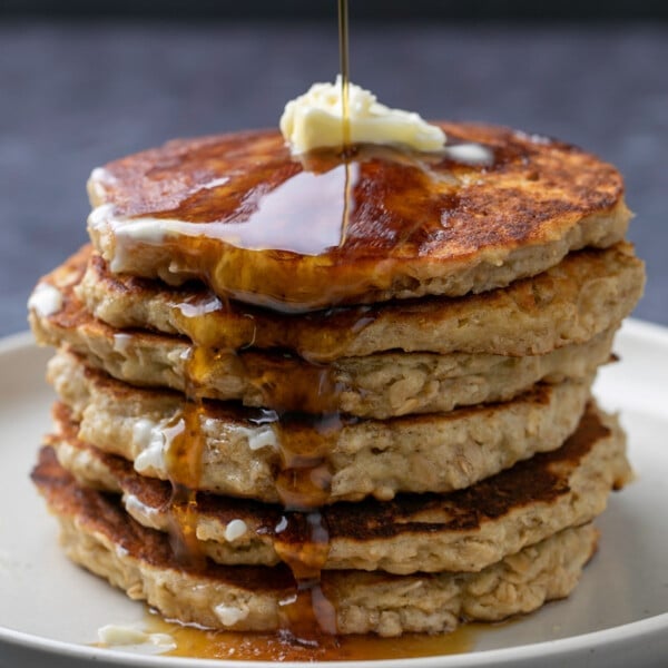 stack of 7 gluten free oatmeal pancakes with pat of butter on top and syrup pouring down side