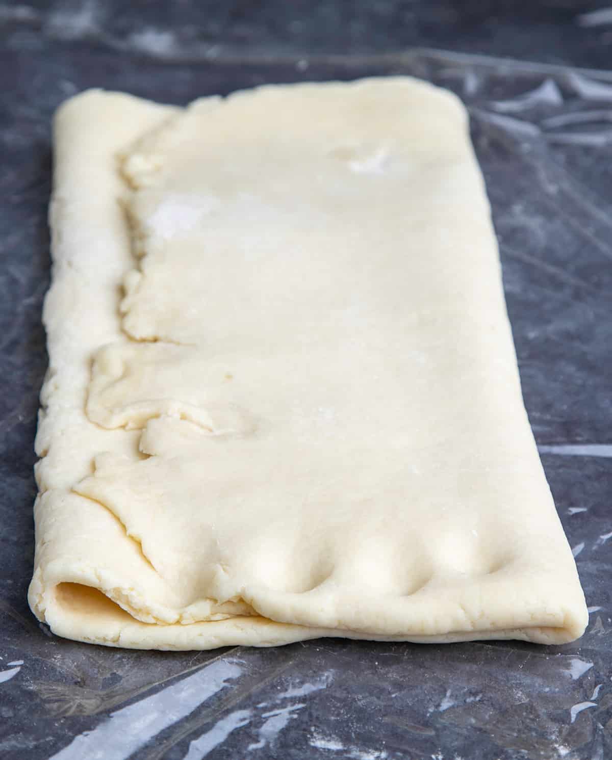 Rectangular folded over raw gluten free croissant pastry dough with 4 notches on plastic