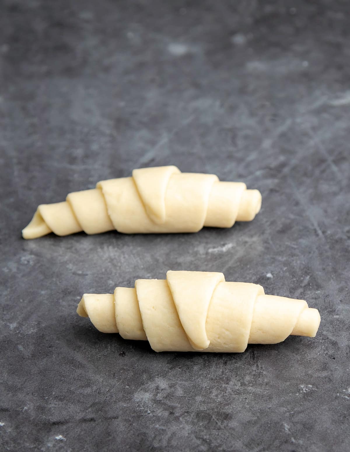 Two raw shaped gluten free croissants on gray background