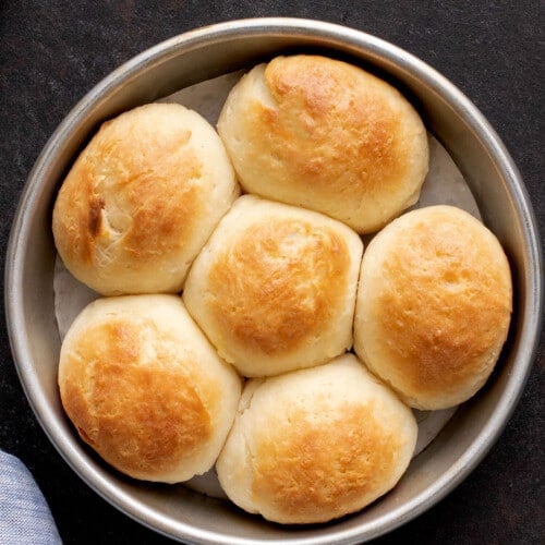 6 light brown soft gluten free dinner rolls in round baking dish