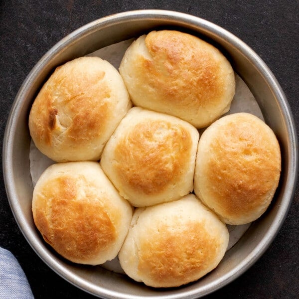 6 light brown soft gluten free dinner rolls in round baking dish