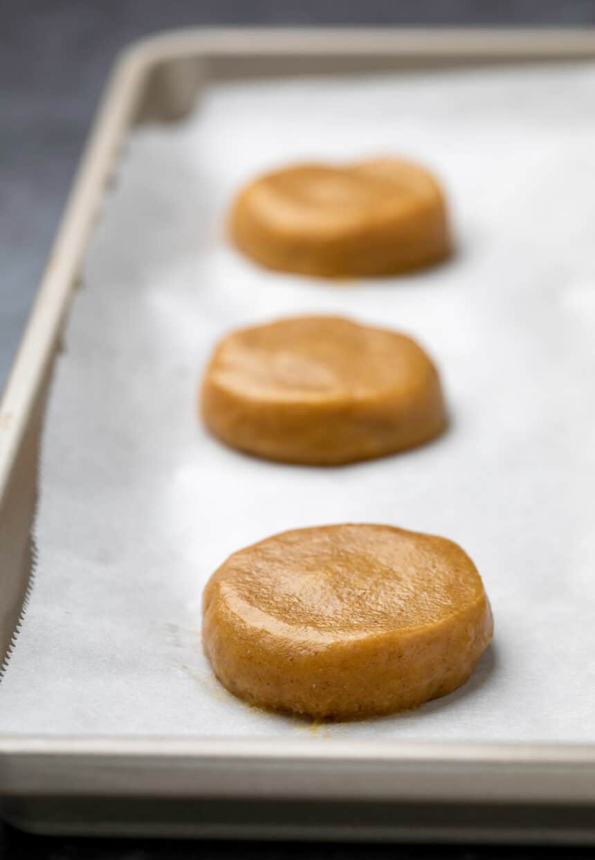 3 disks of raw pumpkin cookie batter on white paper on tray