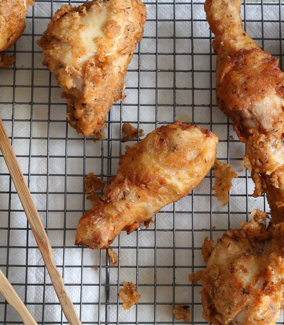 Overhead view of gluten free fried chicken on wire rack with tongs