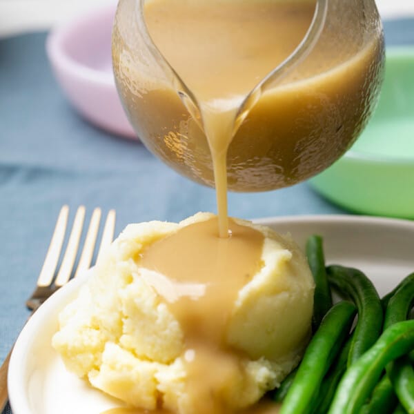 gluten free turkey gravy pouring from glass gravy boat onto mashed potatoes on white plate with fork