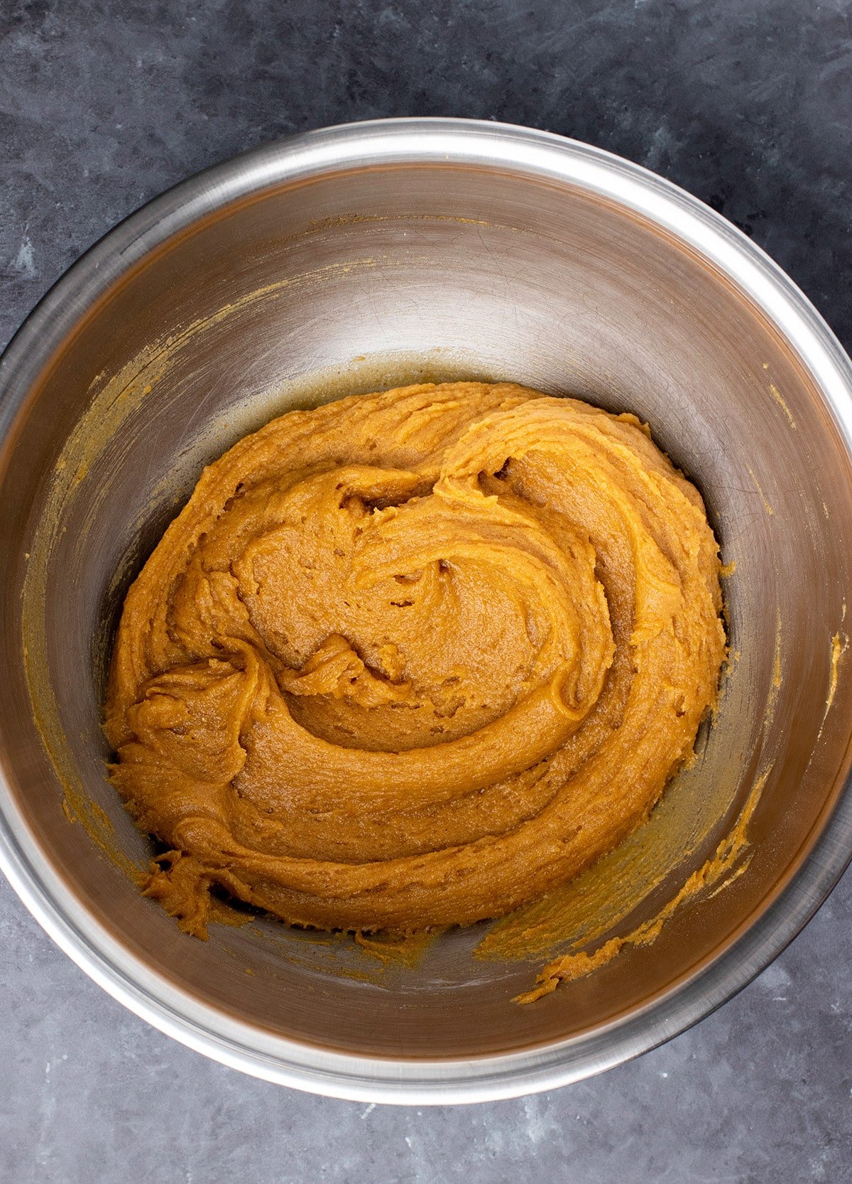 Orange colored cookie batter in large metal mixing bowl.