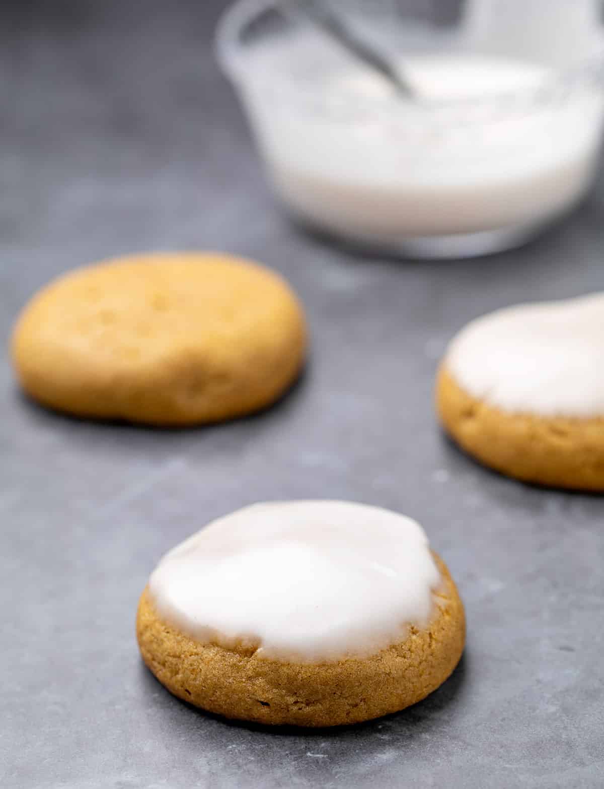 Pumpkin cookies with icing and without with bowl of icing in background
