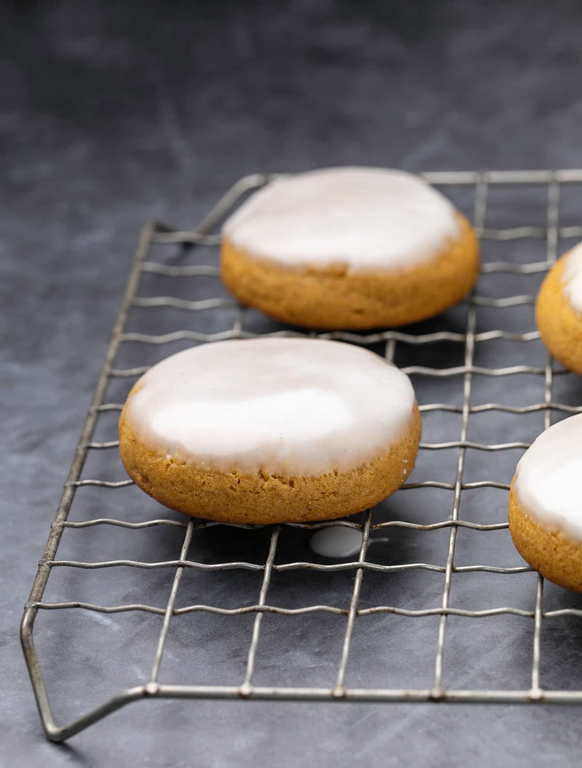 Pumpkin cookies with white icing dripping on wire rack