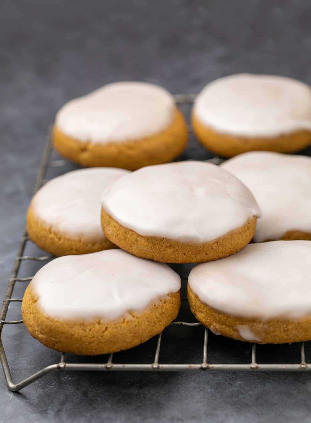 Stack of pumpkin cookies with white icing on wire rack