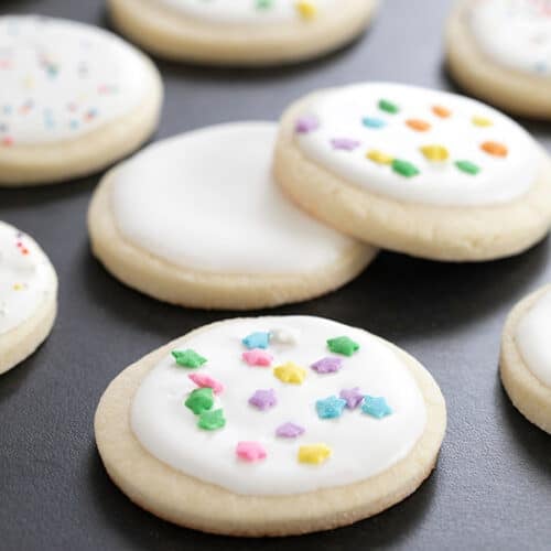 round cutout sugar cookies with white royal icing with star-shaped sprinkles on black surface