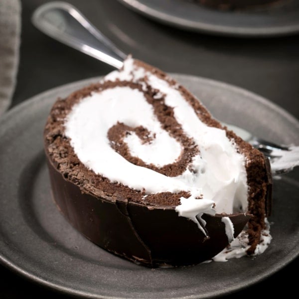 slice of gluten free Swiss roll cake with white filling on small pewter plate with fork