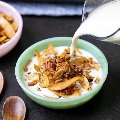 Milk pouring into granola from glass jar into green bowl